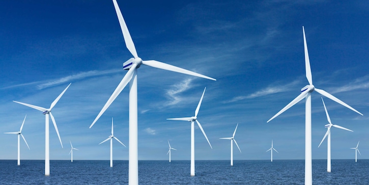 Multiple white offshore wind turbines against a blue sky.