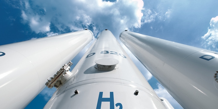 Ground up perspective of three tall white hydrogen storage tanks against a blue sky.