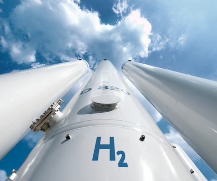 Ground up perspective of three tall white hydrogen storage tanks against a blue sky.