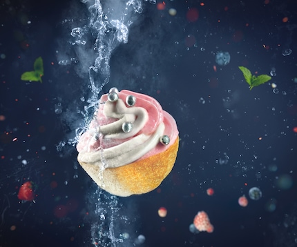 An artistic photograph of a cupcake with colorful sprinkles being partly frozen with liquid nitrogen on a dark background