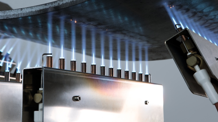 Close up of three LINDOFLAMM special burners each showing a row of twelve extremely focused white flames heating a curved metal part.