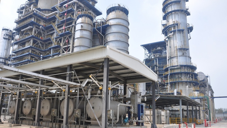 The infrastructure of an oil refinery showing several dull, grey structures like towers and tanks.
