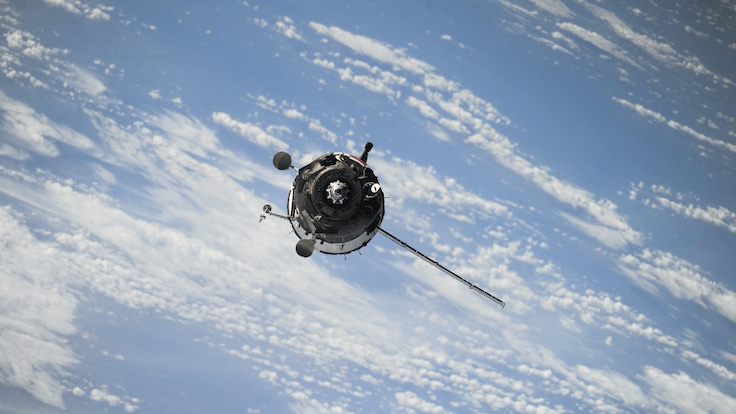 Aerial view of NASA satellite high in orbit in space with clouds in background.