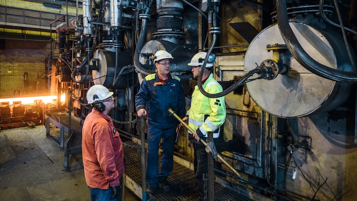 Three workers in personal protective equipment talking in front of a steel burner at OVAKO factory, Sweden.